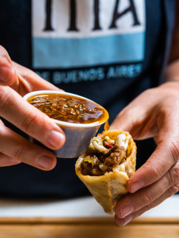 Vertiendo chimichurri en una empanada Tita  scaled